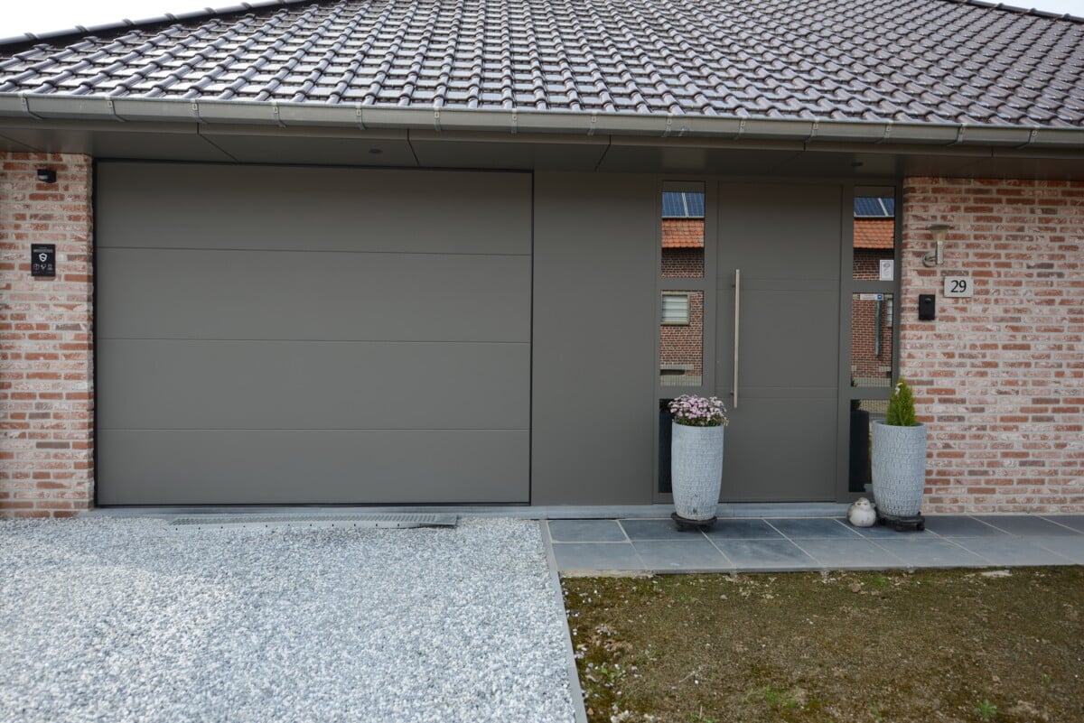 Moderne grijze aluminium voordeur en garagepoort van woning met bakstenen gevel en tegeldak