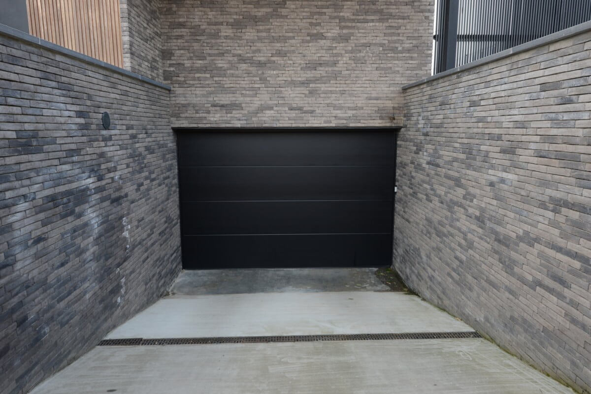 Moderne zwarte aluminium garagepoort in betonnen garage omringd door grijze bakstenen muren