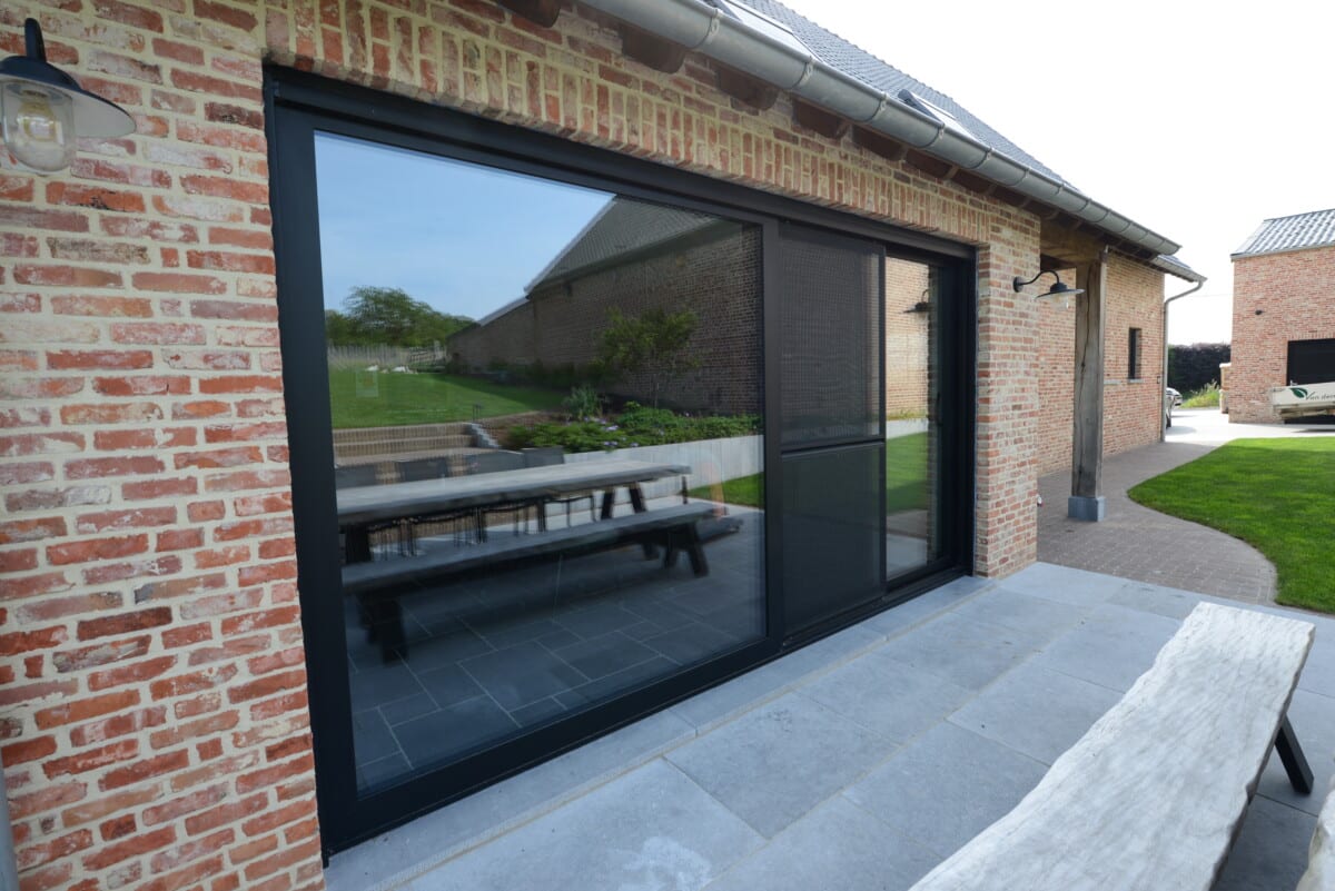Modern bakstenen huis met grote zwarte aluminium schuiframen die uitzicht bieden op tuin en terras met picknicktafel