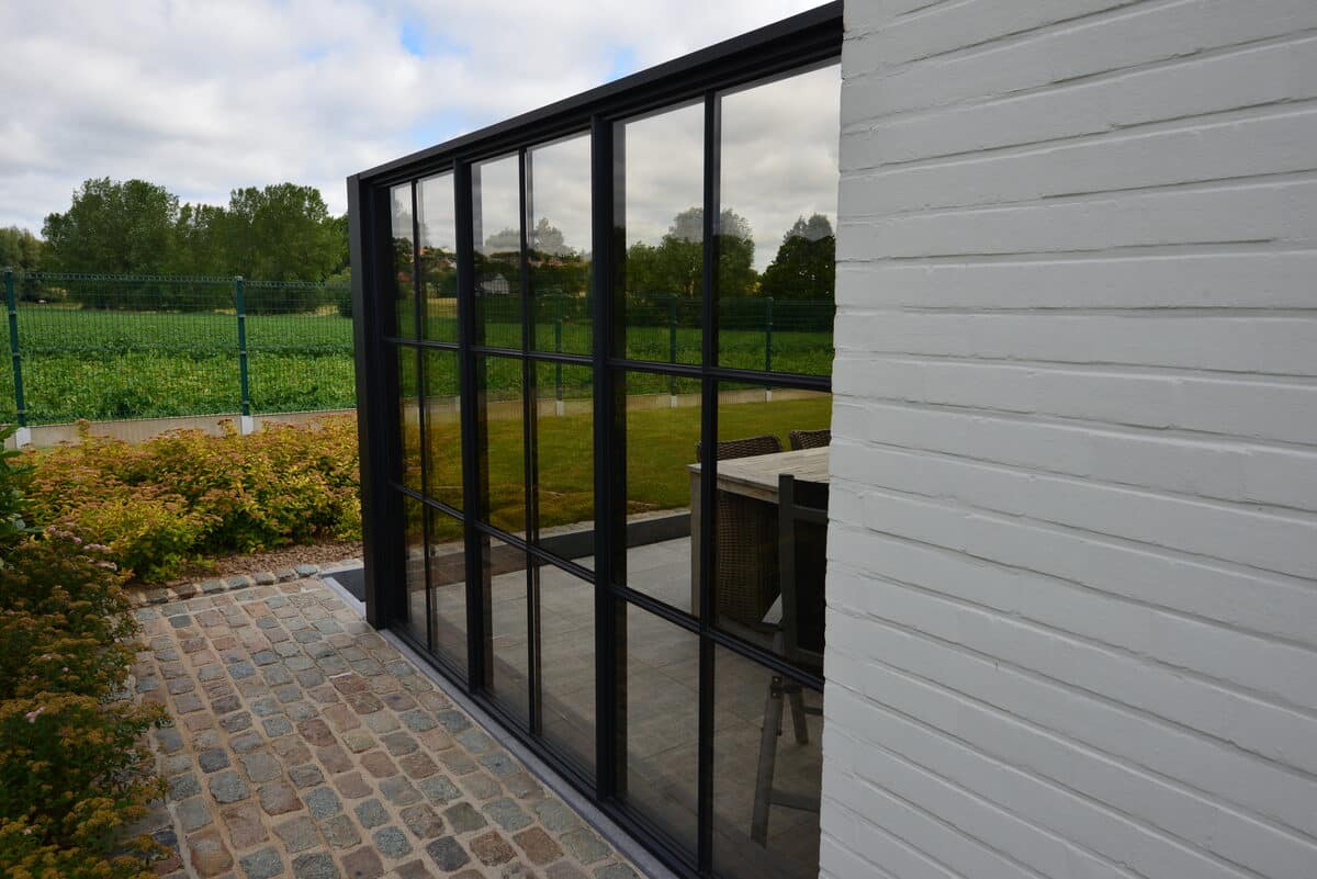 Zwarte steellook glaswand langs een wit geschilderde bakstenen gevel