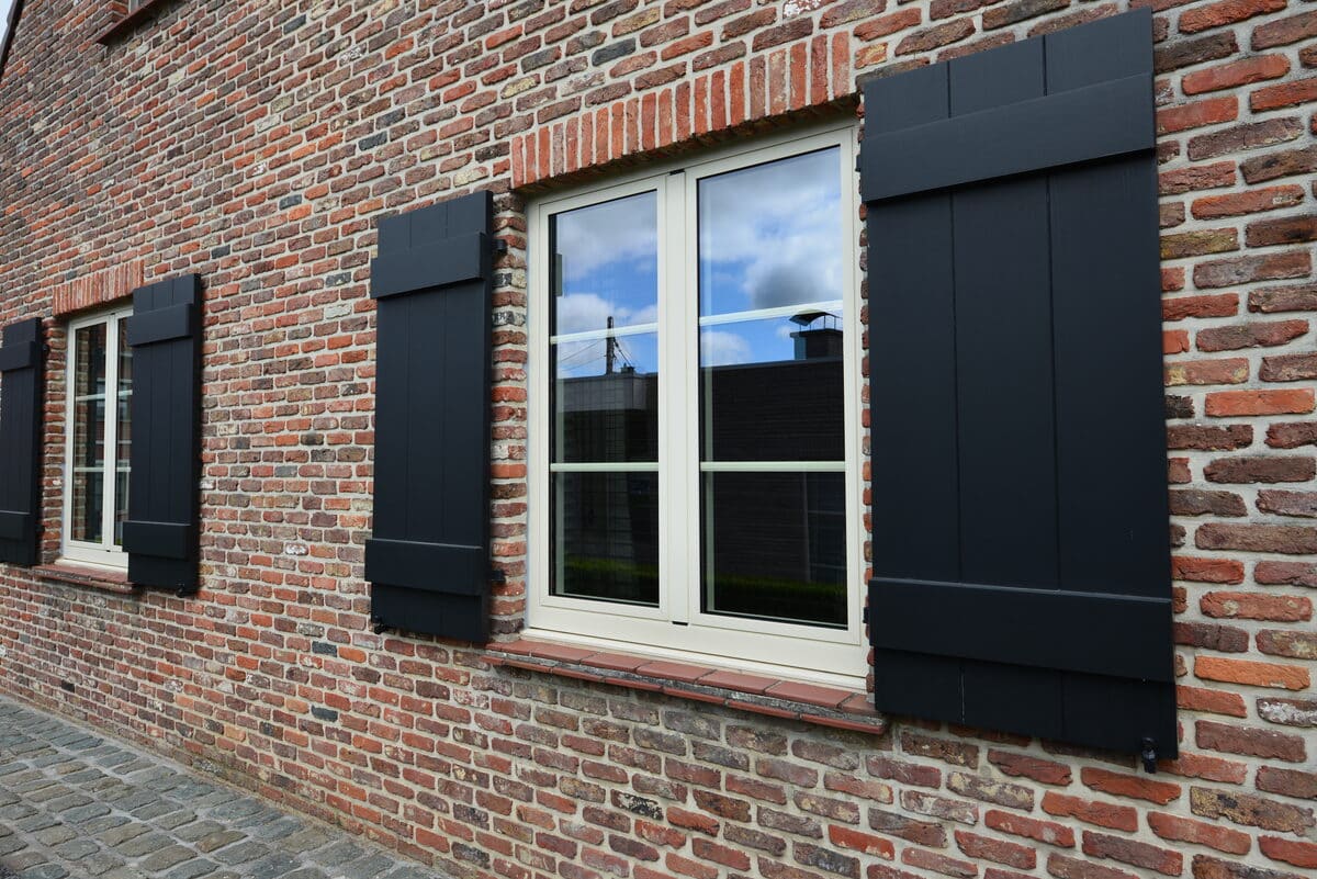 Crèmekleurig aluminium raam met zwarte luiken in een bakstenen gevel