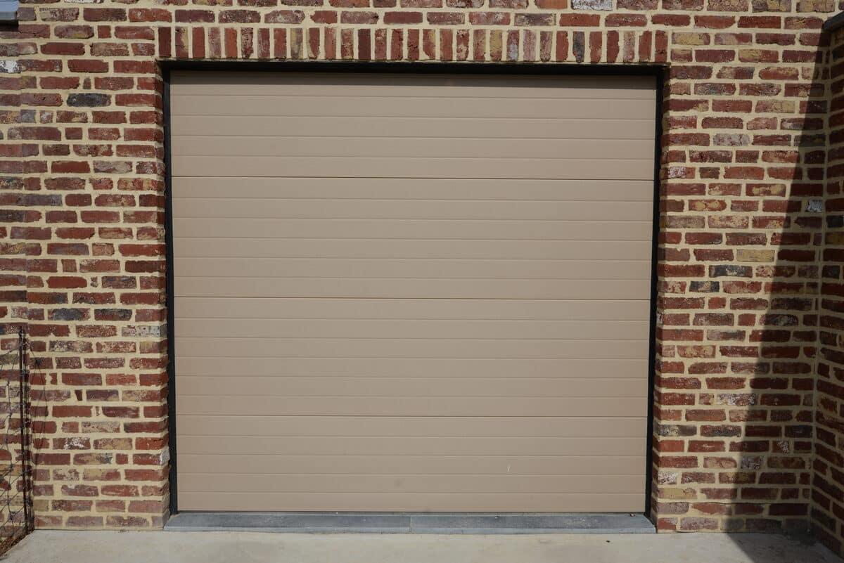Beige sectionale garagepoort in een bakstenen gevel
