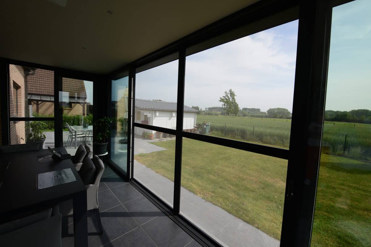 Zicht vanuit een veranda door zwarte aluminium schuifdeuren op de velden